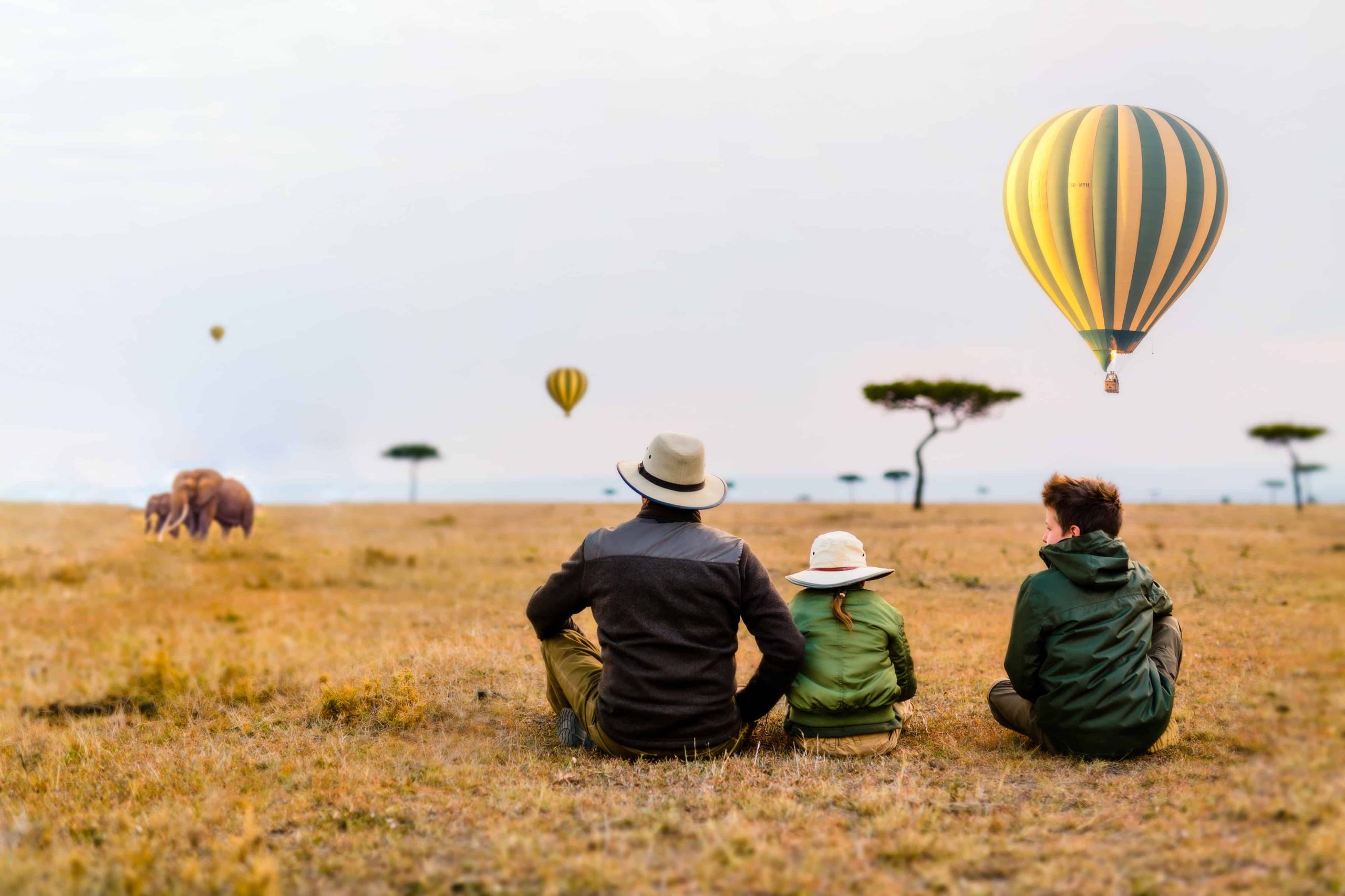 Travellers sitting in the grass watching hot-air balloons rise over the plains
