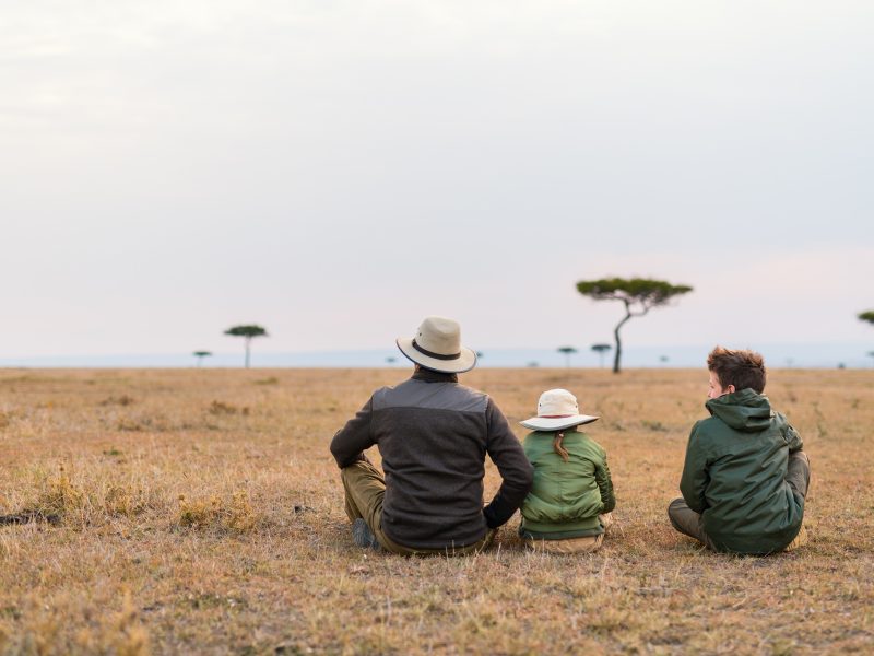 Family of father and kids on African safari vacation enjoying views over Masai Mara in Kenya