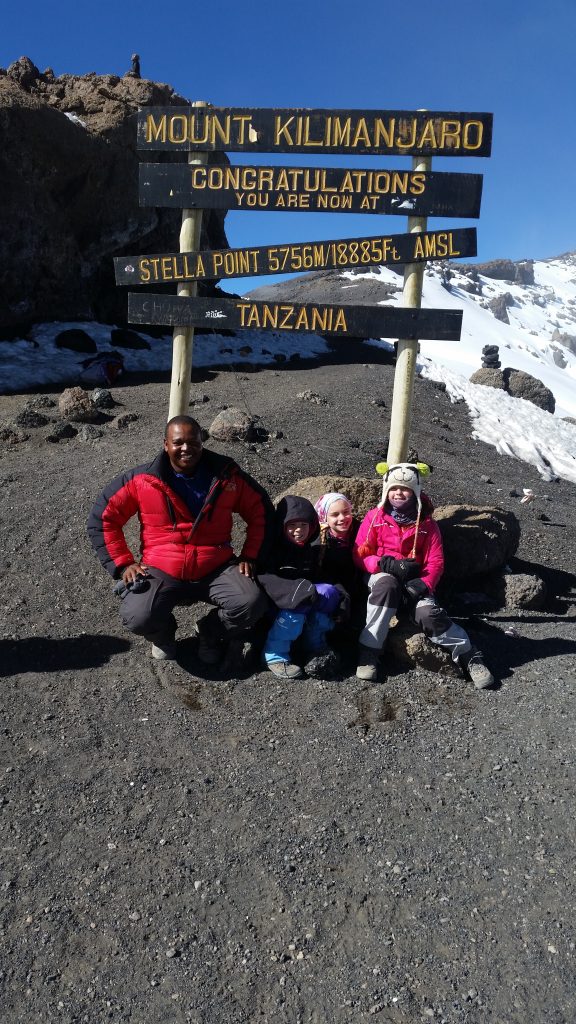 Gabriel Nkini with three young children beneath the Stella Point sign, 5,756 m, on Mount Kilimanjaro