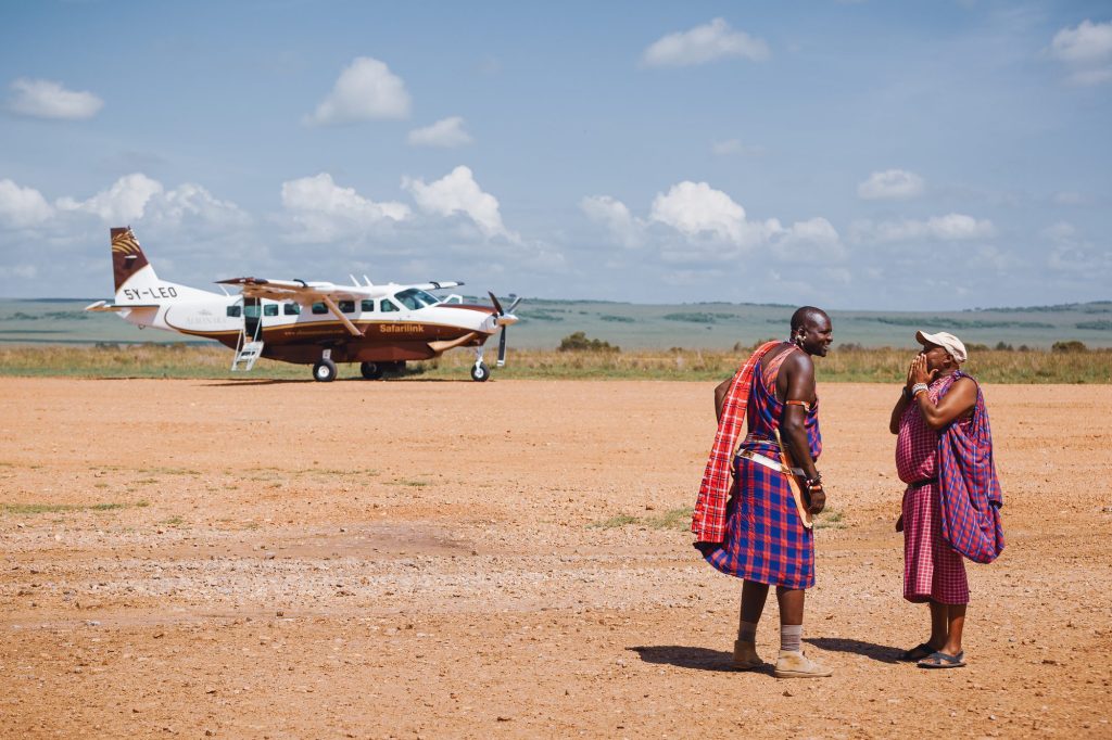 A light aircraft on a dirt airstrip with two men in traditional dress in the foreground